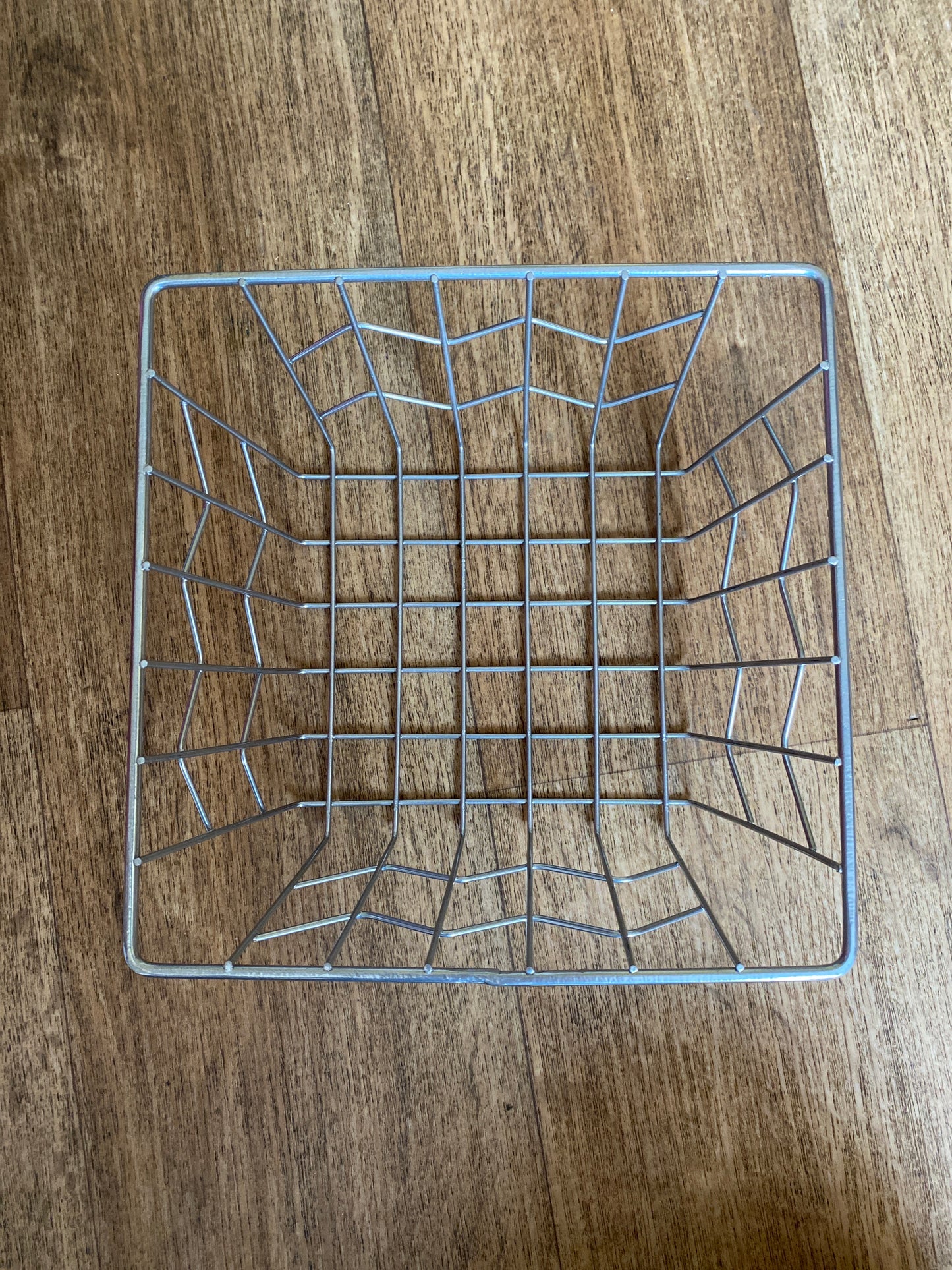 A square metal basket, viewed from the top down, on a wooden floor. 