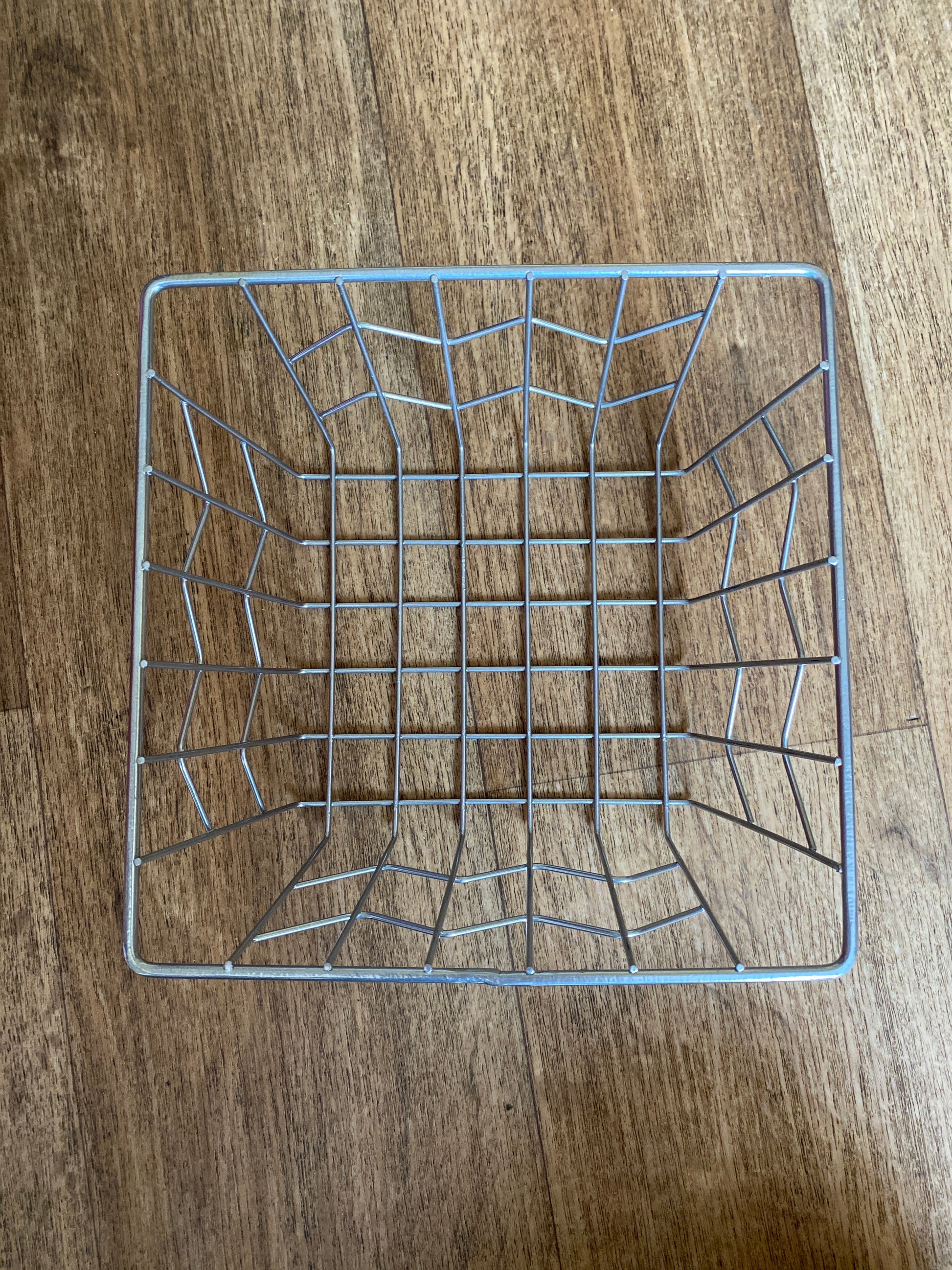 A square metal basket, viewed from the top down, on a wooden floor. 