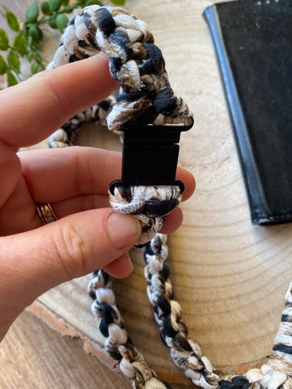 A hand holding a black plastic safety break clasp, which is part of a macrame phone holder lanyard, made with animal print t shirt yarn. 