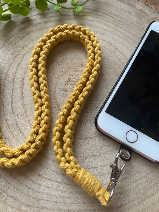 An iPhone on a wooden board with a yellow macrame phone lanyard attached to it with a metal clasp. 