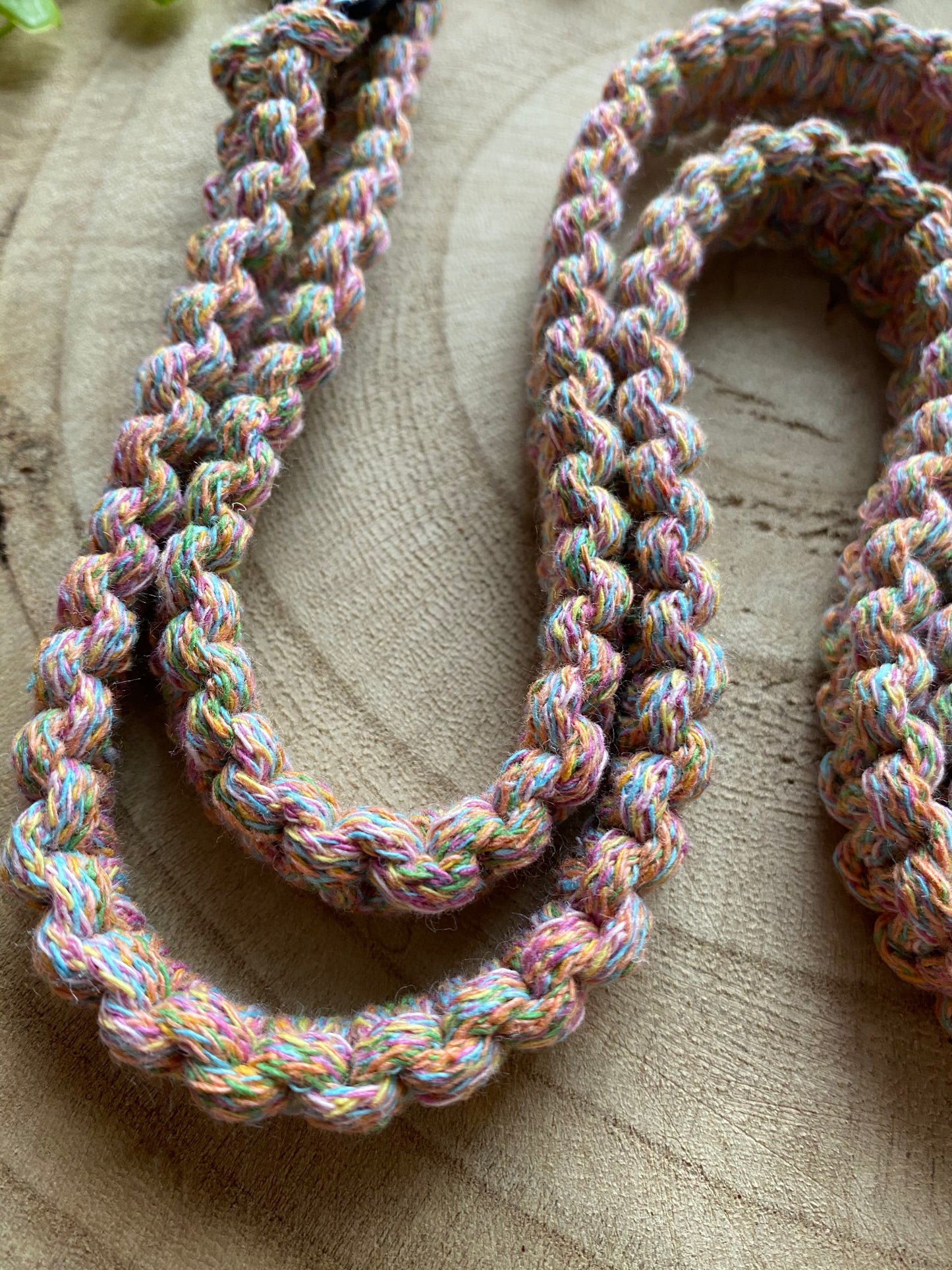 A close up of a neatly knotted macrame phone lanyard made with rainbow yarn, on a wooden surface. 
