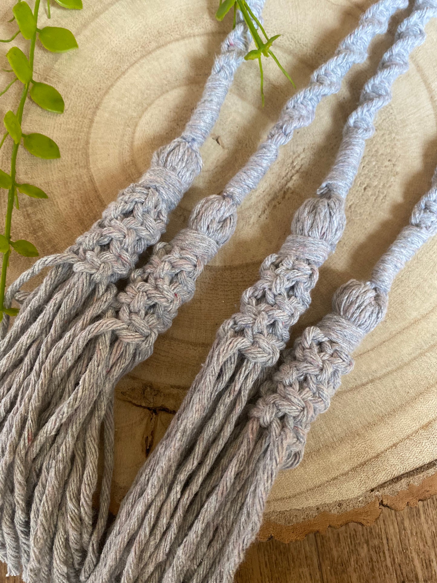 A close up of a pair of knotted macrame tassel tiebacks made with light grey yarn. 