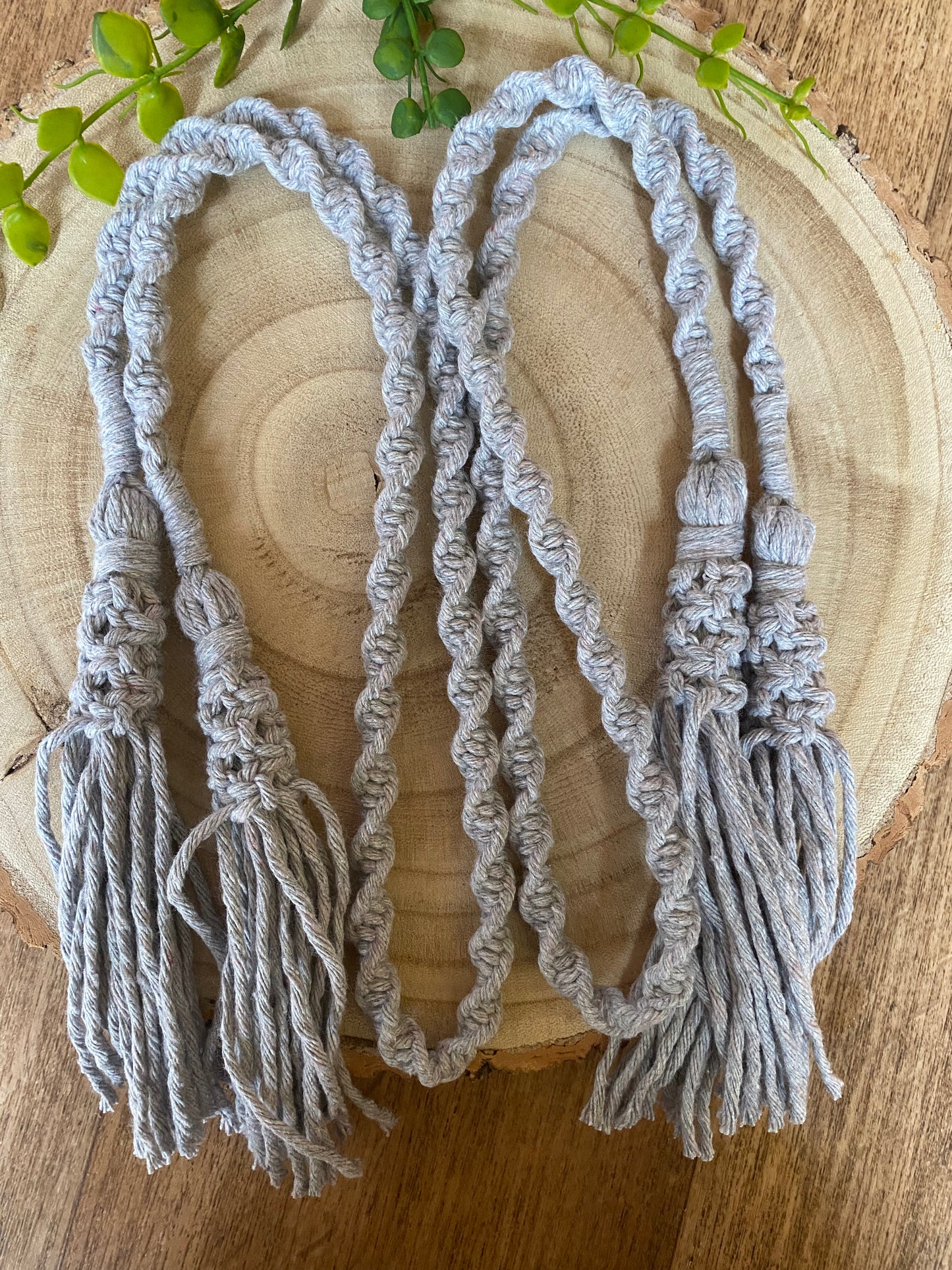 A pair of knotted macrame tassel tiebacks, made with light grey cotton yarn, laid out on a wooden surface. 
