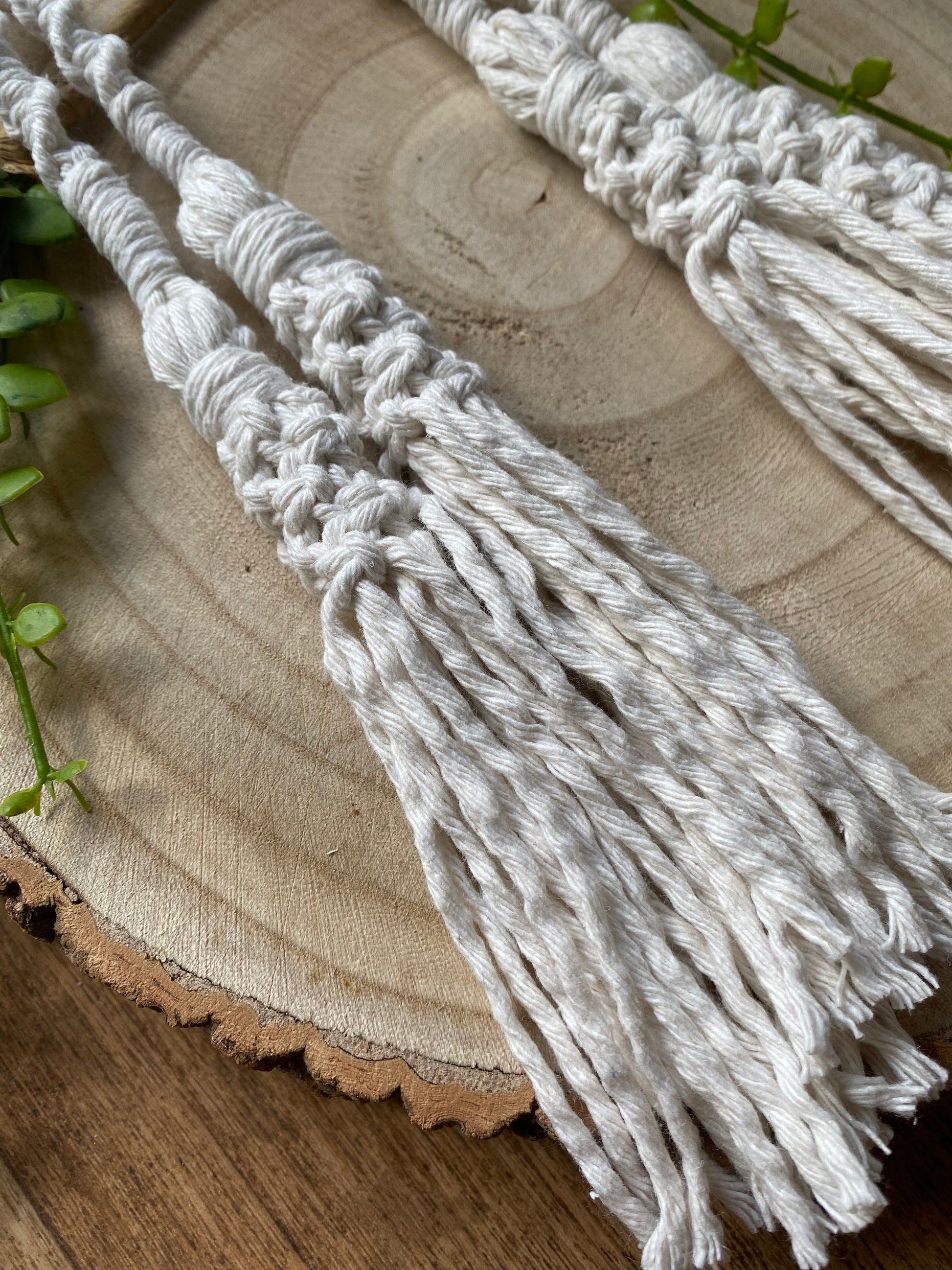 A close up of the tasseled ends on a pair of knotted macrame curtain tiebacks, made with natural yarn a wooden surface. 