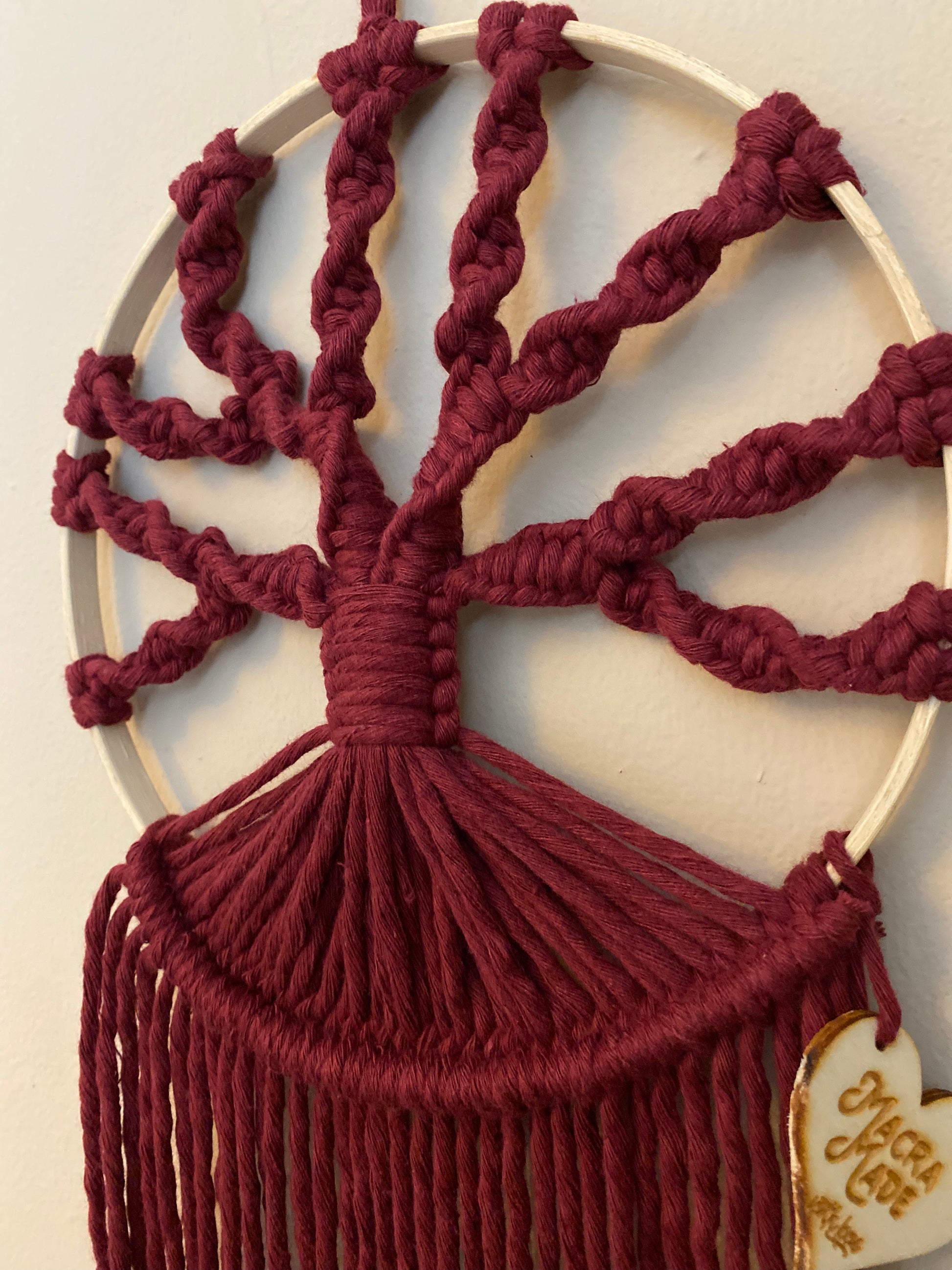 A close up view of a macrame tree of life wall hanging made on a circular wooden hoop with deep red knotted yarn, in the shape of tree branches. 