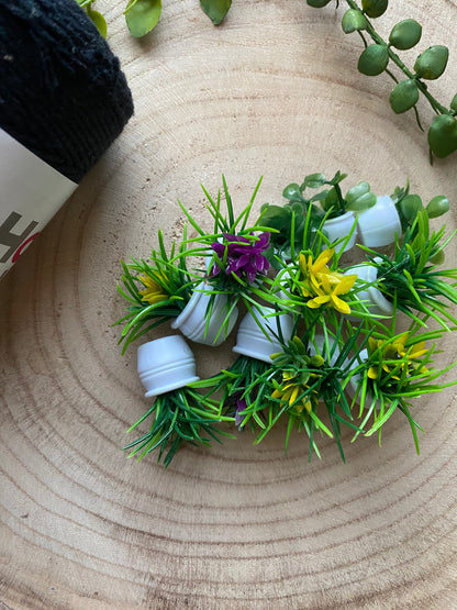 A small selection of mini artificial plants of various shapes and colours, laid together on a wooden surface next to a skein of black yarn.