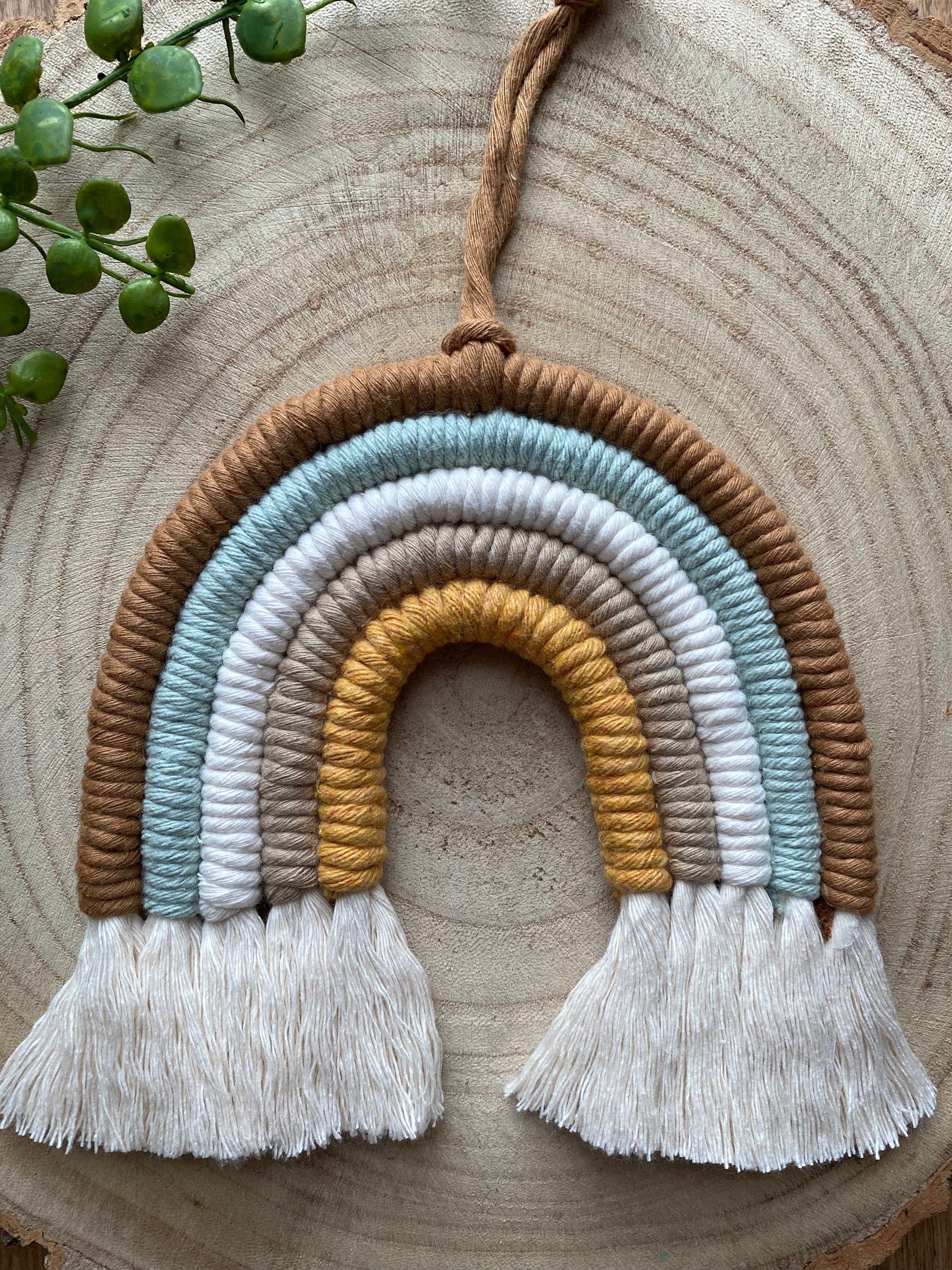 A handmade Neutral Rainbow decoration by Macra-Made-With-Love made with coloured yarns in neutral shades, displayed on a wooden surface. 