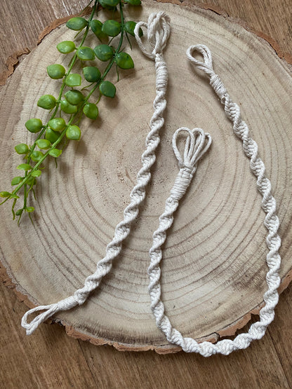 Two macrame plant hanger extensions of different lengths, each made with natural cotton yarn, laid out next to each other on a wooden surface.