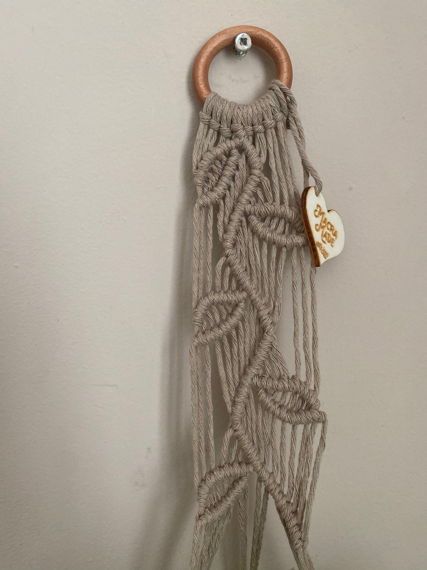 Close up of a neutral coloured macrame plant hanger with falling leaf knotted pattern and a wooden ring. 