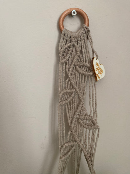 Close up of a neutral coloured macrame plant hanger with falling leaf knotted pattern and a wooden ring. 