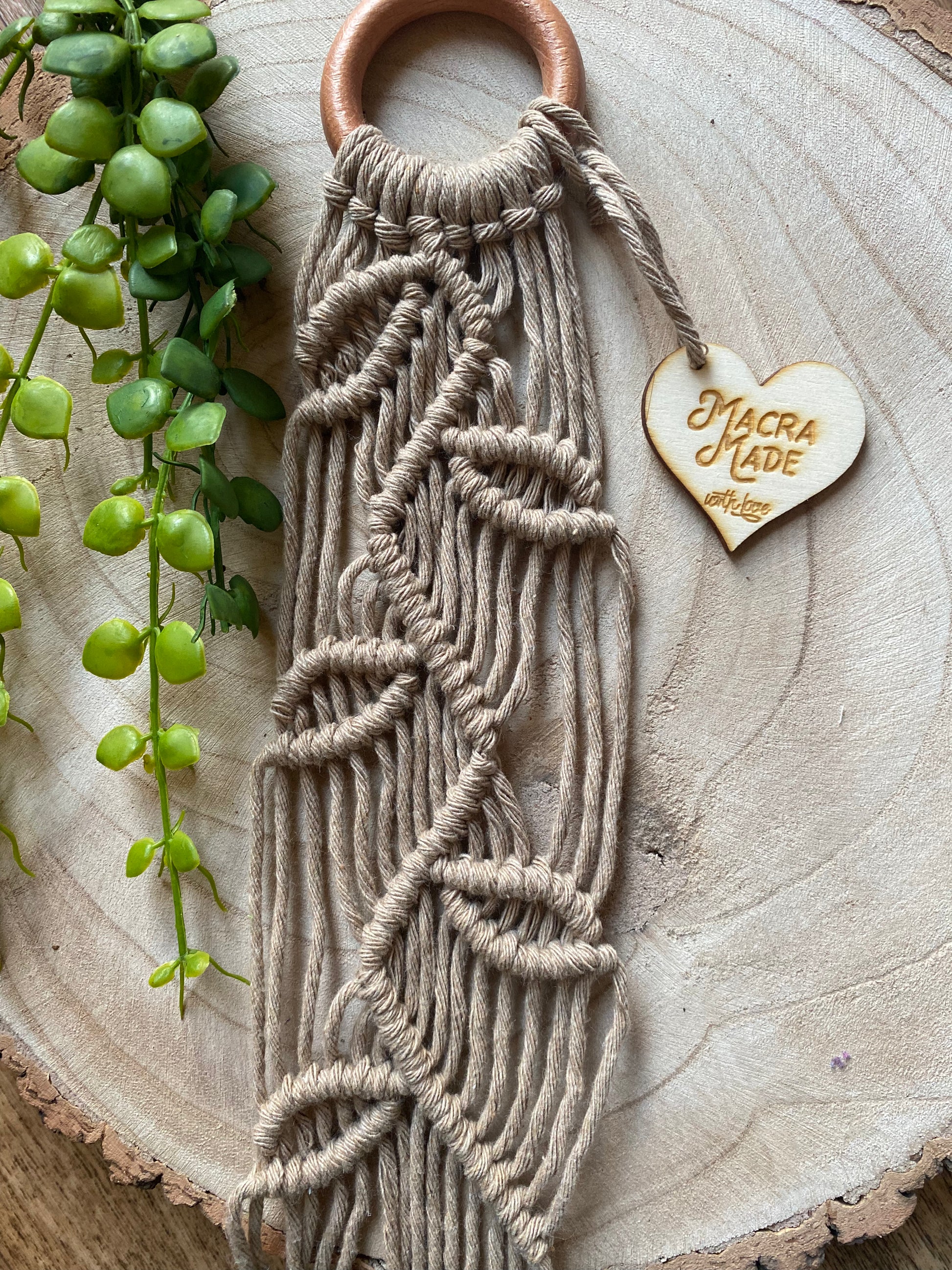 Close up of a neutral coloured macrame plant hanger with falling leaf knotted pattern and a wooden ring. 