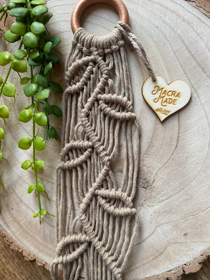 Close up of a neutral coloured macrame plant hanger with falling leaf knotted pattern and a wooden ring. 